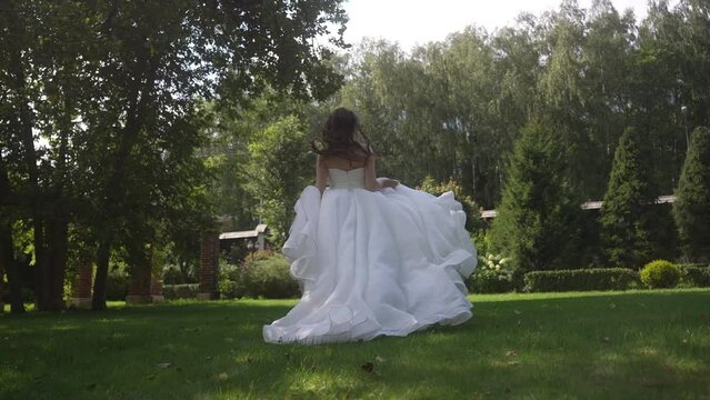 A happy bride in a wedding dress running through a picturesque park landscape