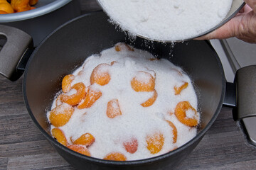 Sugar being poured over the layers of fruit and sugar in the saucepan