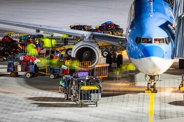 Fototapeta premium Baggage ground handling on the airport ramp. Workers loading a passenger airlplane with lots of baggage and cargo.