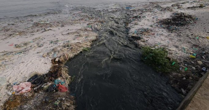 Tilt-up. Stinking effluent sewage water and plastic pollution flowing into the ocean.  