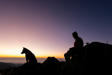 Silhouette of a man hiking with his dog against Orange Sunset Sky in Nature Landscape