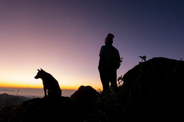 Silhouette of a man hiking with his dog against Orange Sunset Sky in Nature Landscape