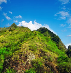 Fototapeta na wymiar Mountain, green and natural landscape with blue sky, summer and calm clouds on peak at travel location. Nature, cliff and sustainable environment with earth, forest and tropical holiday destination