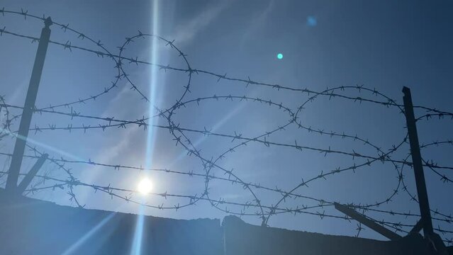 Sharp barbed wire against blue sky and sunlight background, control fence along the concrete wall perimeter for protection from criminals escape or illegal immigration, prison or concentration camp