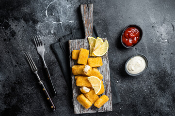 Golden roast Fish Sticks Fingers with sauce on a wooden board. Black background. Top view