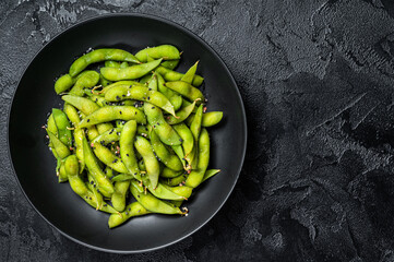 Boiled Edamame Soy Beans with sea salt in a plate. Black background. Top view. Copy space