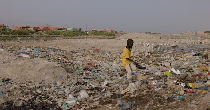 Slow motion. Young Black African boy playing amongst horiffic plastic pollution