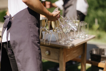 A waiter holds a pile of glasses by the legs. Catering, restaurant, serving, serving, serving welcome drink, alcoholic beverages. A solemn event