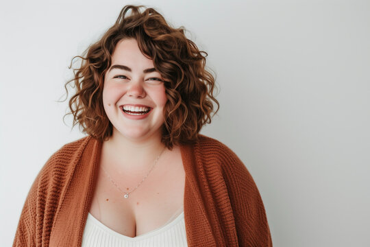 Radiant plus-size woman with curly hair and cardigan smiling joyfully against a light background.