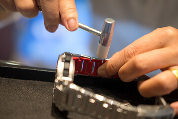 A watch pin being installed into the watch band with a hammer and a watch band holder