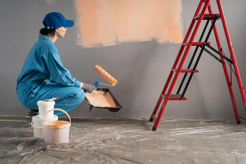 Side view of painter with cap squatting ready painting a wall with paint roller. repair, building...