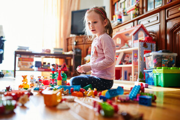 Adorable preschooler girl sitting on the floor and playing with colorful construction blocks - obrazy, fototapety, plakaty
