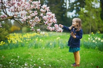 Adorable preschooler girl enjoying nice spring day in park during magnolia blooming season