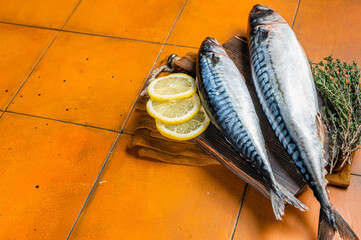 Raw mackerel fish, Scombrus with herbs and spices on wooden board. Orange background. Top view....