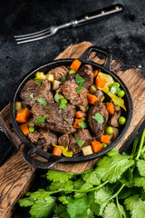 Beef stew with potato, carrot and herbs in a skillet. Black background. Top view