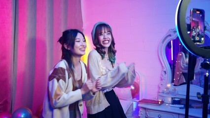 Happy Asian generation z woman friends vlogger influencer content creator enjoy and fun using smartphone online live streaming viral video cover dance on social media application in bedroom at home.
