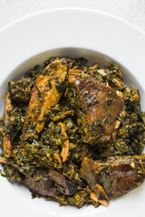 Nigerian vegetable soup with fish and bush meat in a white plate, afang soup in a large dinner plate, traditional edikang ikong soup in a white dish	