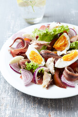Salad with hard-boiled eggs, tomatoes, lettuce, red onion and smoked mackerel on bright wooden background. Close up.	