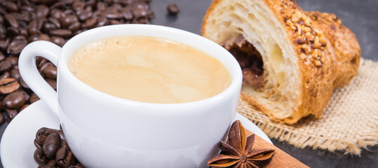 Coffee in white cup with anise and cinnamon and fresh baked croissant