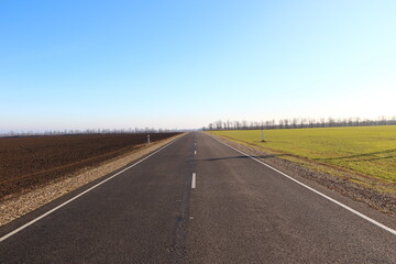 Asphalt road near agricultural fields and blue sky on a backround