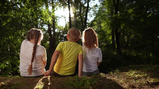 children sit on the banks of the river. happy family childhood dream concept. a group of little children sit together by the river and talk. kids lifestyle spend time outdoors in nature in the forest