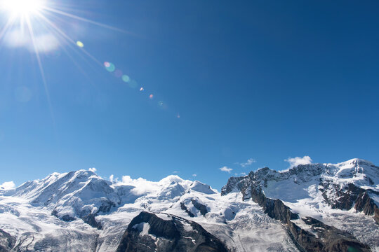 View summer 2021 of Monte Rosa massif with Dufourspitze, Lyskamm (Silberbast), Breithorn in Pennine Alps on border of Switzerland and Italy near Zermatt; sun bright in blue sky with some lens flare
