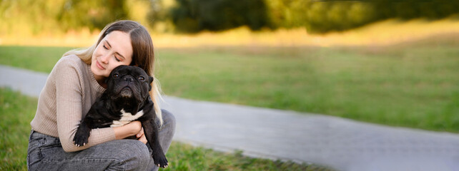 Banner, woman hugs her black French bulldog tightly while walking in park. Concept of helping...