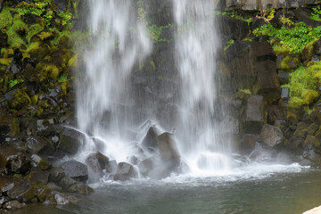 Close up view of low shutterspeed water falling on rocks in the plunge pool of the Svartifoss waterfall in Skaftafell in Vatnajökull National Park, Iceland with a base of sharp basalt hexagonal column