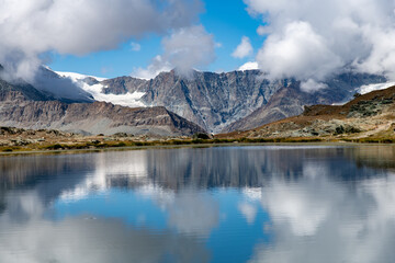 Panoramic view over the water of the Riffelsee near Zermatt, Switzerland towards Monte Rosa massif in eastern part of the Pennine Alps just north of the Matterhorn with mountains reflected in water