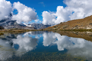 Panoramic view over the water of the Riffelsee near Zermatt, Switzerland towards Monte Rosa massif in eastern part of the Pennine Alps just north of the Matterhorn with mountains reflected in water