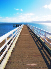Obraz premium Mountain, ocean and wooden pier on island with blue sky, tropical landscape and travel in Indonesia. Beach, vacation and relax on wood bridge, jetty or dock with sea water, clouds and summer in Bali
