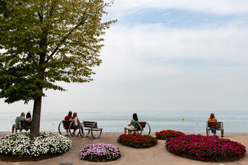 View from the shoreline of one of the lakes in Italy with a number of people on park benches...