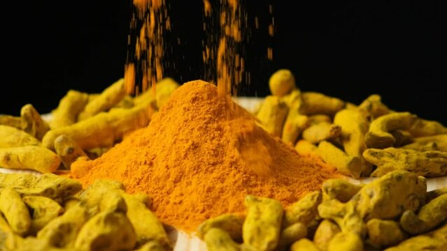 Turmeric powder sprinkled on wooden dish with powder and dry turmeric root, slow motion.
