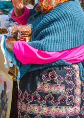 The colorful outfit of the seller of cookies and sweets, holding packages of waffles. Shopping area in Portugal. Only parts of the body are visible.