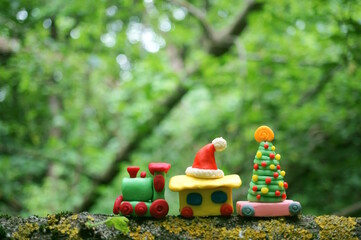 A toy train with a Christmas tree and a Santa Claus hat in the forest. Christmas toys made of plasticine.