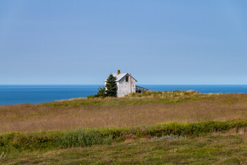 White abandoned, dilapidated farmhouse with some farmland on the north coastline of Iceland with panoramic view of the ocean against a blue sky in the background