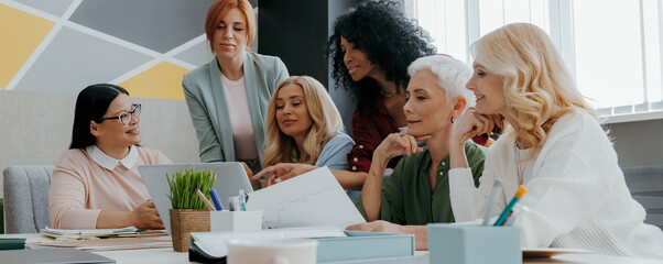 Group of mature women looking at laptop while discussing business in the office together - 749383979