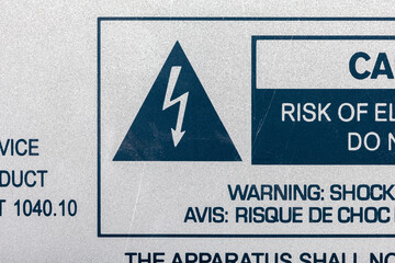 A close-up view of a bilingual warning label detailing the risk of electrical shock from a machine...