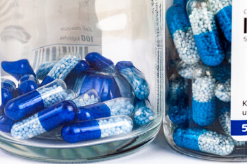 Blue white capsules with granules inside in transparent glass jars, showcasing pharmaceutical products, drugs, medicine generic pills tablets closeup detail, nobody. Buying selling meds concept