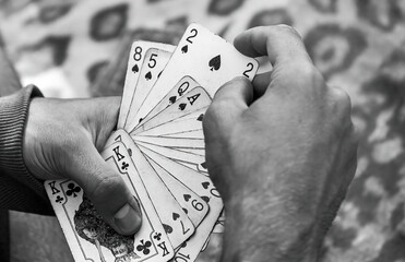 Black and white dramatic close-up of hands holding a variety of playing cards spread, poker,...