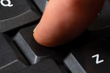 Close-up shot of a finger mid-action as it presses an unlabeled black key on a modern computer keyboard. Taking action, any key button press, anonymous user input simple abstract concept, one person