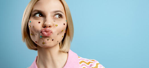 Young woman with colorful rhinestones over her face making a face against blue background - 749393108