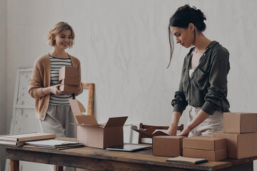 Two confident businesswomen preparing packages for delivery in warehouse - 749393971