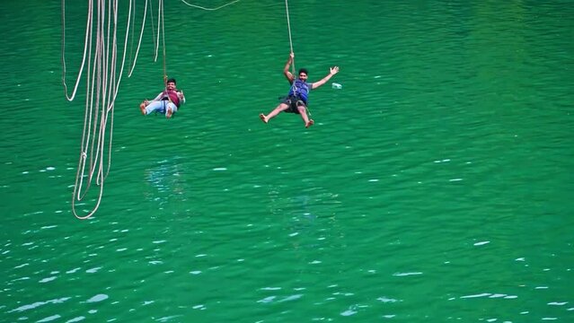 Two young tourist having fun at zipline, sliding over the river, slow motion footage.