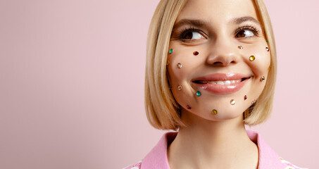 Happy young woman with colorful rhinestones over her face standing against pink background - 749402553