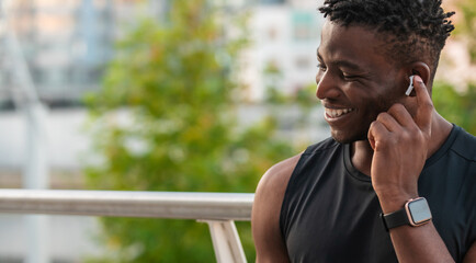 Handsome African man adjusting his headphones and smiling while resting after sport training - 749404765