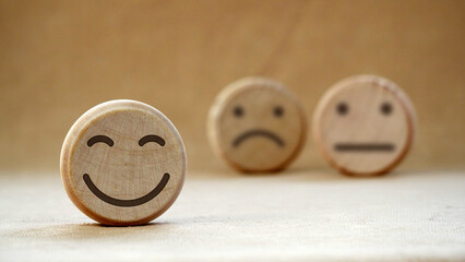 Wooden round with carved happy and angry faces, International Day of Happiness concept, customer reviews, emotional intelligence, emotional control balance, feedback rating, mental health assessment.