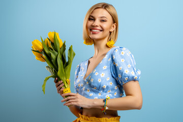 Happy young woman holding bunch of tulips and smiling against blue background - 749406542