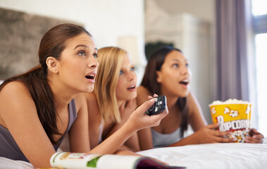 Fototapeta na wymiar Surprise, watching tv and friends eating popcorn in bedroom for streaming show, relax or amazed together at home. Television, food or group of women with shock in bed for movie, film and wow at party