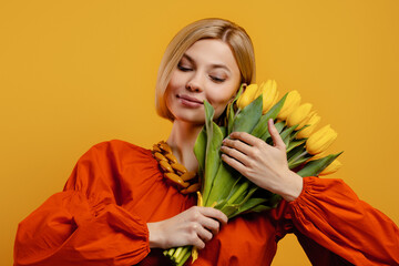 Attractive young woman holding bunch of tulips near face and against yellow background - 749411995